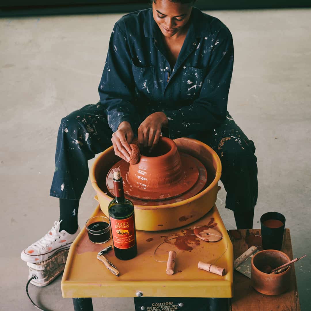 Young artist making pottery in the art studio keeping bottle of 1000 Stories wine on the pottery turn table