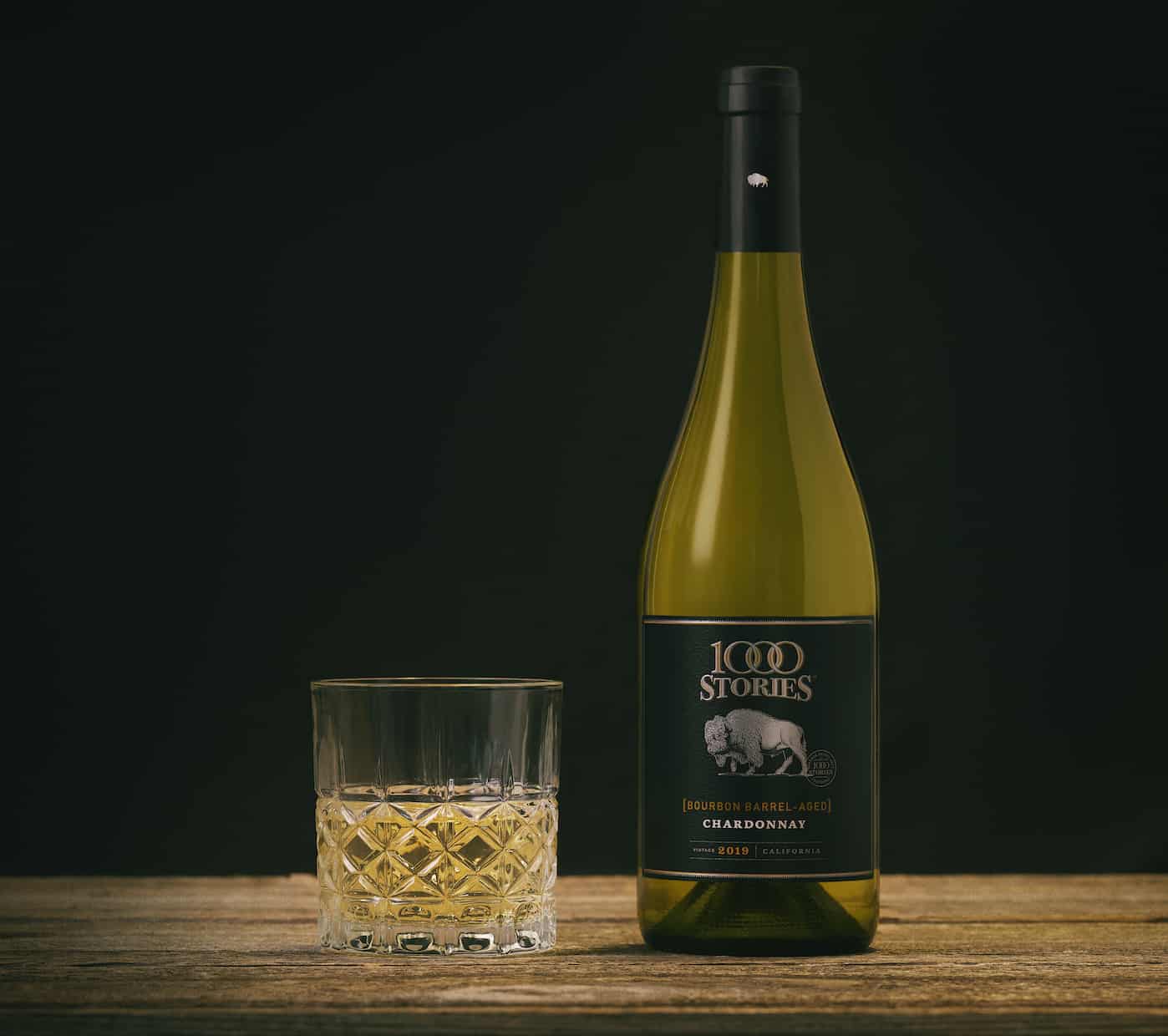 A glass of white wine sits next to a bottle of 1000 Stories Chardonnay