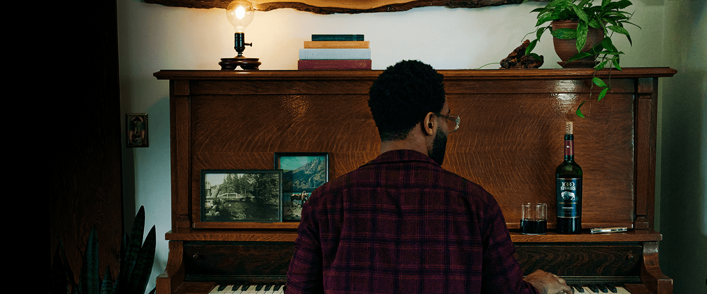 Man plays a piano with a bottle of 1000 Stories bourbon barrel-aged Zinfandel next to him