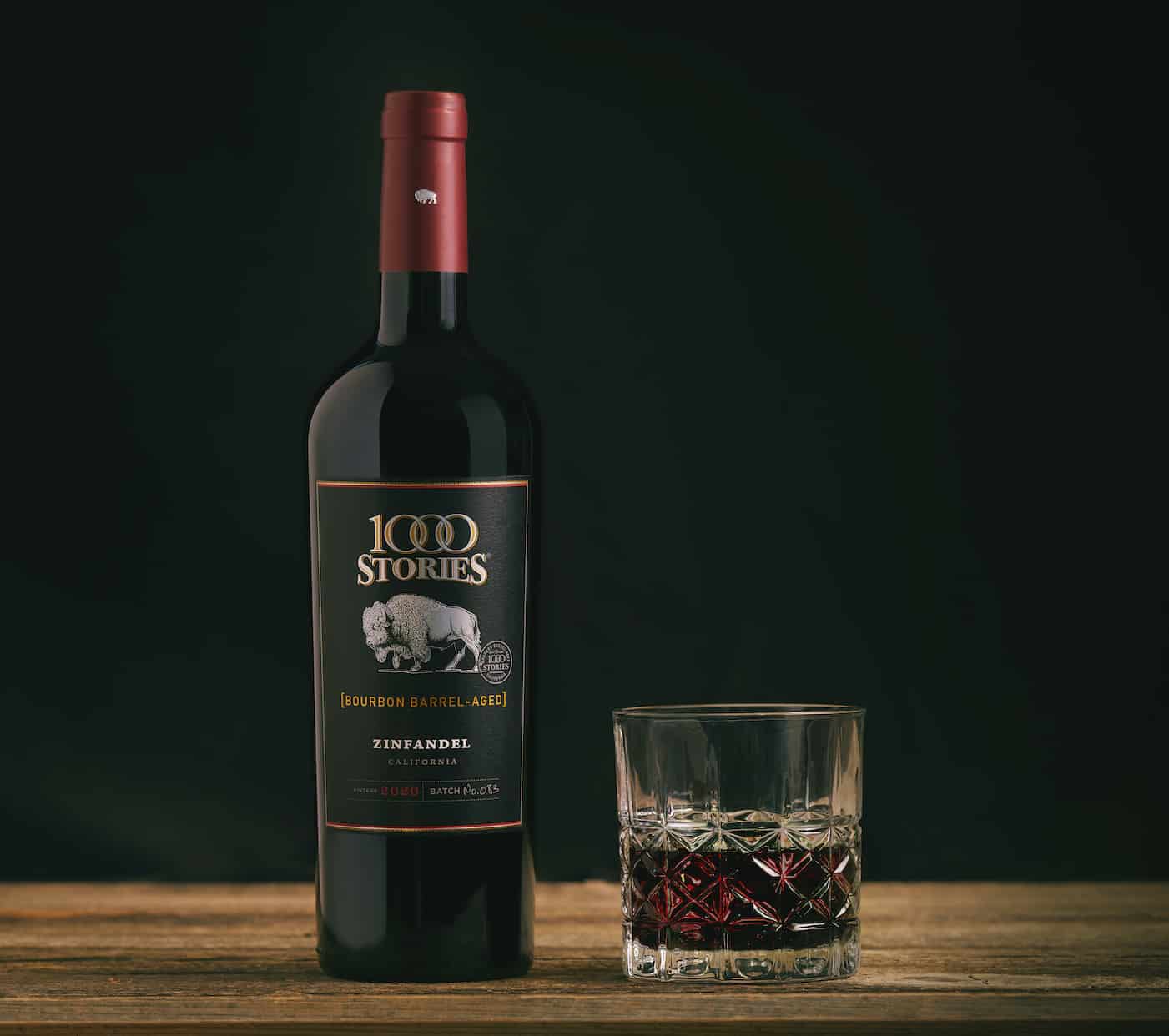 A glass of red wine sits next to a bottle of 1000 Stories bourbon barrel-aged Zinfandel