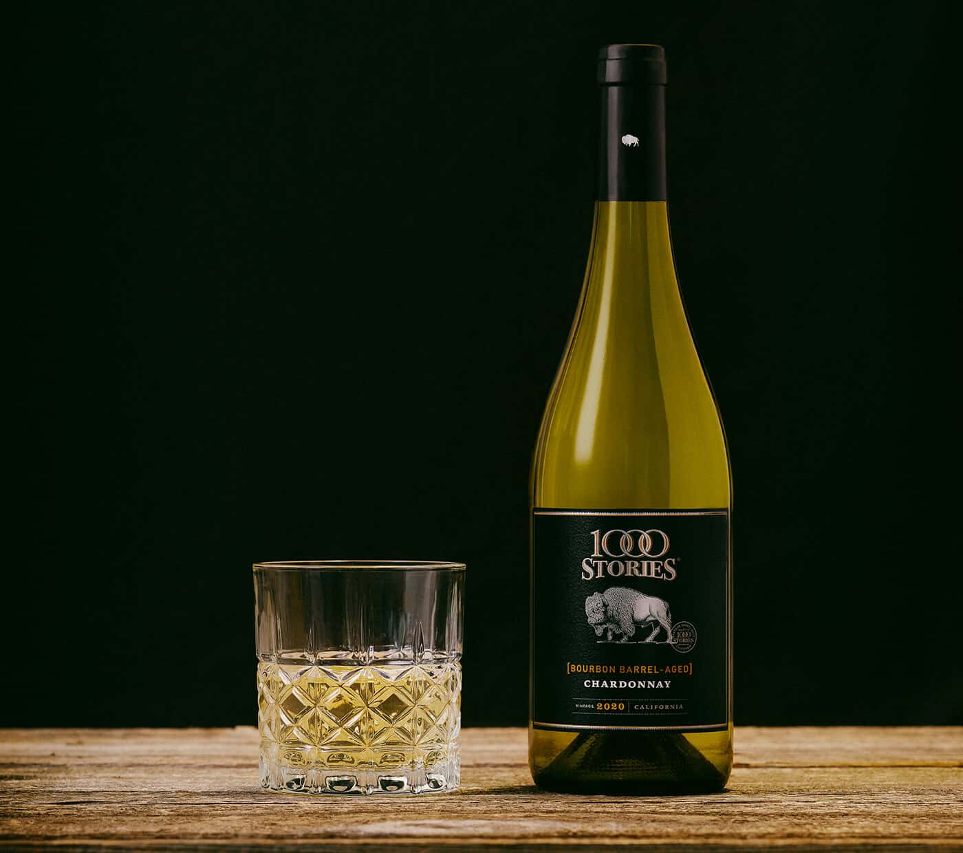 A glass of white wine sits next to a bottle of 1000 Stories 2020 Chardonnay