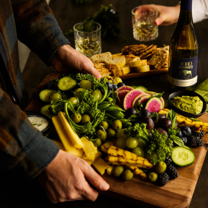 Vegetarian Charcuterie Board featuring American Barrel Aged Chardonnay, crackers, olives, assorted cheeses, berries, broccolini, and radishes for color pops. 